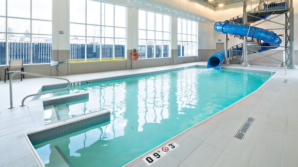 Une piscine intérieure avec un toboggan bleu, de l’eau claire et des repères indiquant la profondeur pour assurer la sécurité.