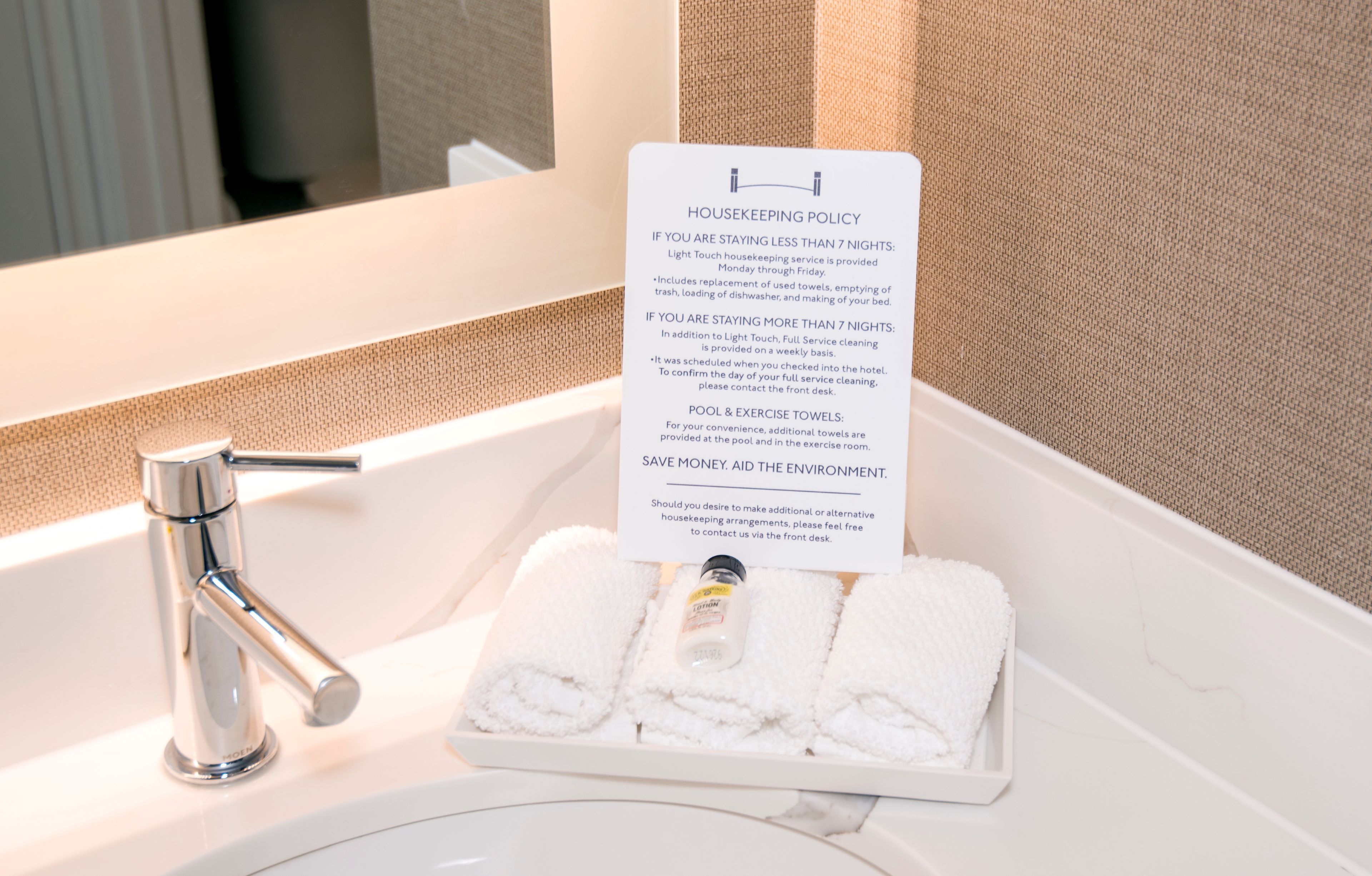 A hotel bathroom sink with a hand towel and a housekeeping policy sign.