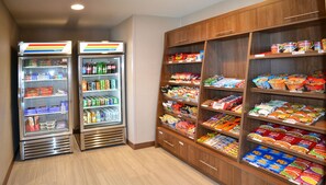 Zona de venta con opciones de bocadillos y bebidas, incluyendo un refrigerador y una estantería con diversos productos.