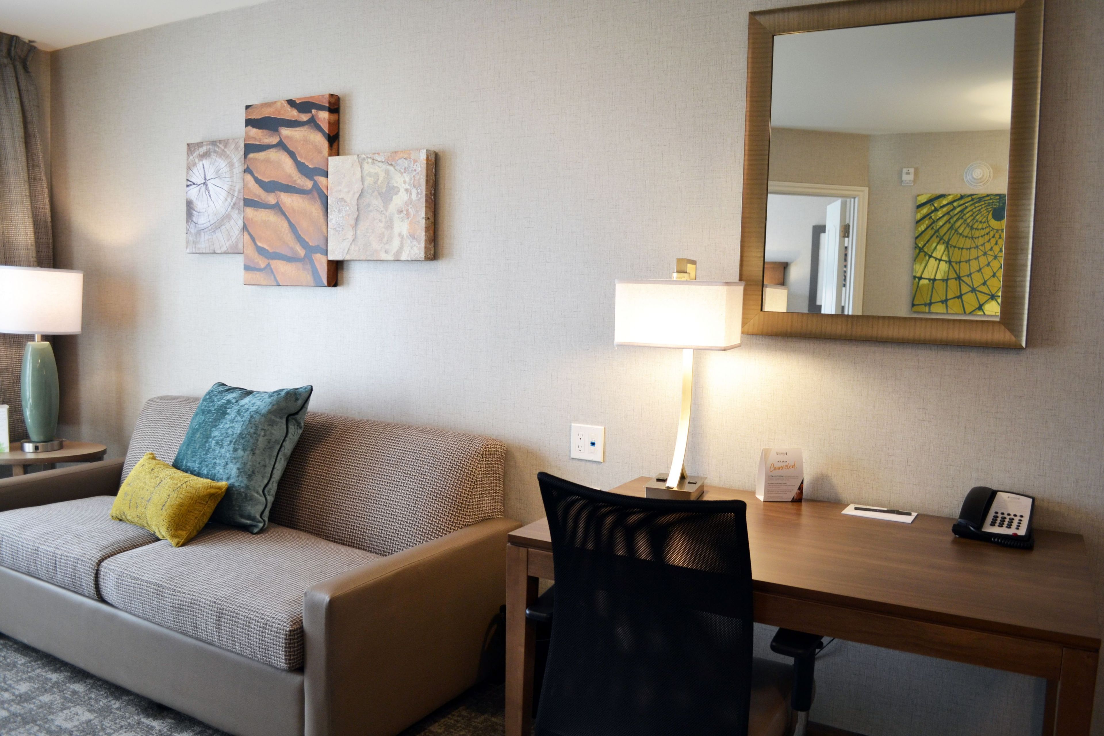 Habitación de hotel con sofá, escritorio, silla, lámpara, teléfono y una obra de arte en la pared.