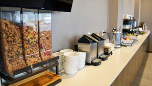 Buffet-alue, jossa on tarjolla erilaisia aamiaismuroja, kahviautomaatti ja pino valkoisia lautasita.