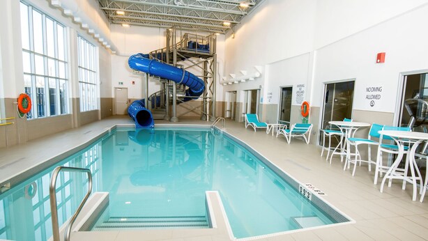 Una piscina interior con un tobogán azul, sillas de descanso y una estación de salvavidas.