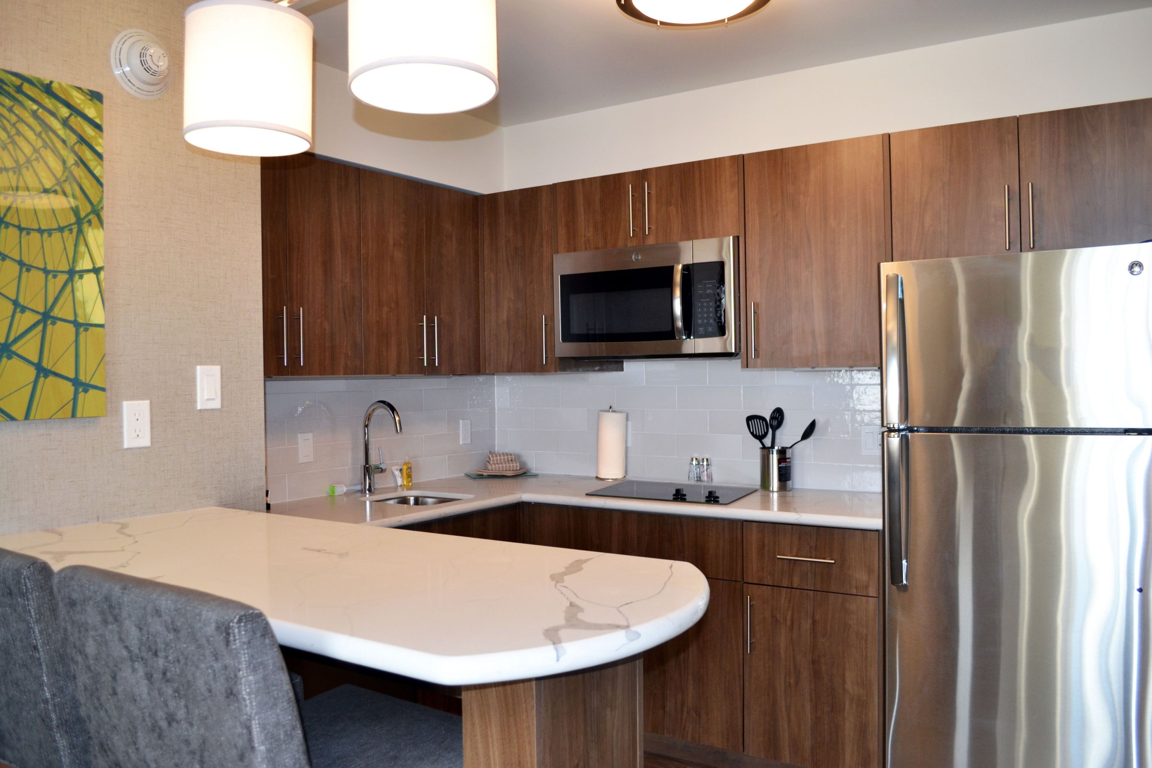 A modern kitchen with wooden cabinets, stainless steel appliances, a marble countertop, and pendant lighting.