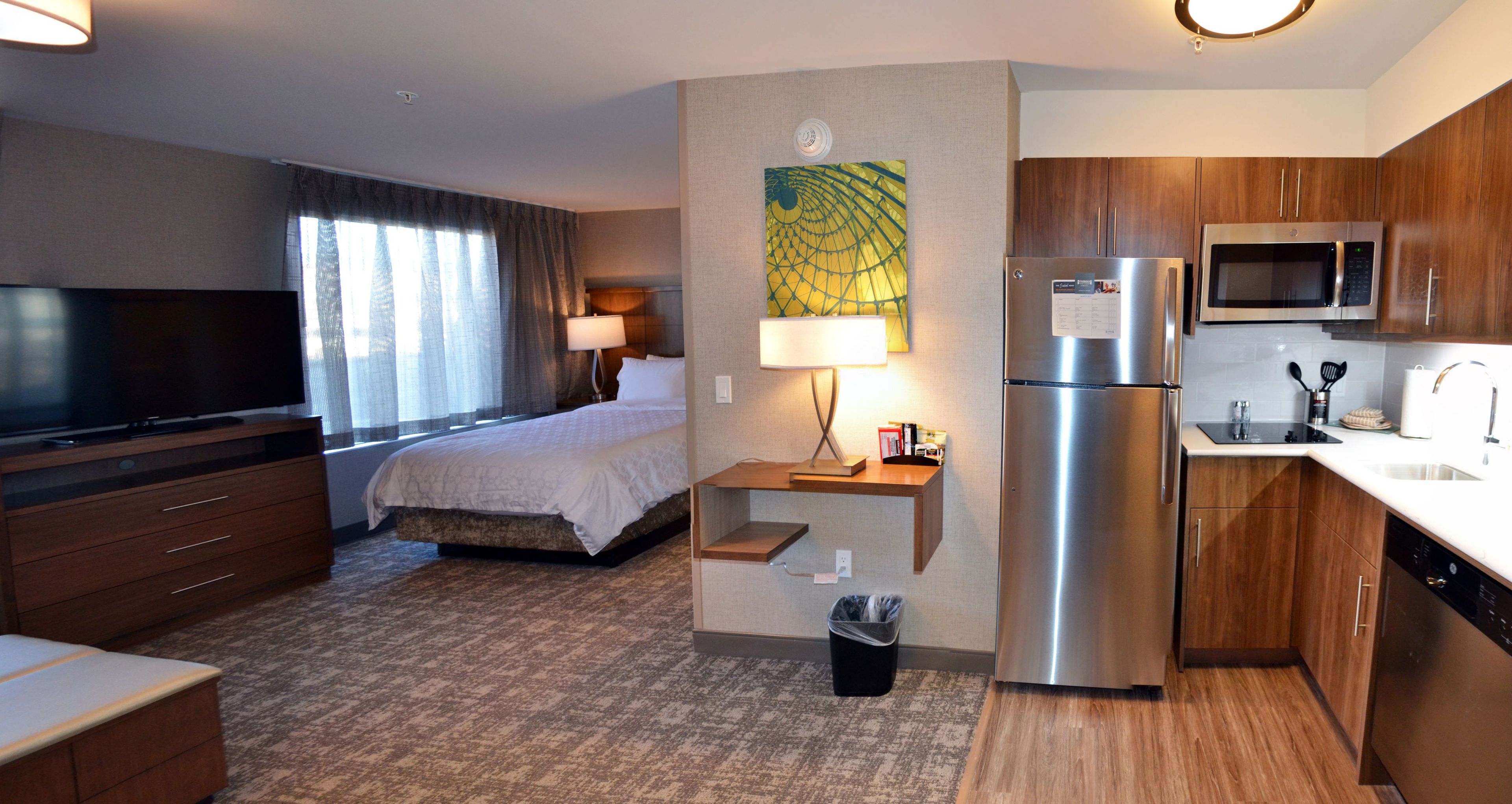 Habitación de hotel con cama, televisor, escritorio con lámpara, refrigerador, microondas y lavamanos.