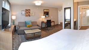 Una habitación de hotel con cama, sofá, escritorio, silla, televisor y baño.