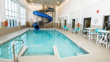Une piscine intérieure avec un toboggan bleu, des chaises longues et un poste de surveillance pour les sauveteurs.