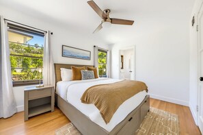 Une chambre à coucher avec un lit, des tables de chevet, un ventilateur de plafond et de grandes fenêtres.