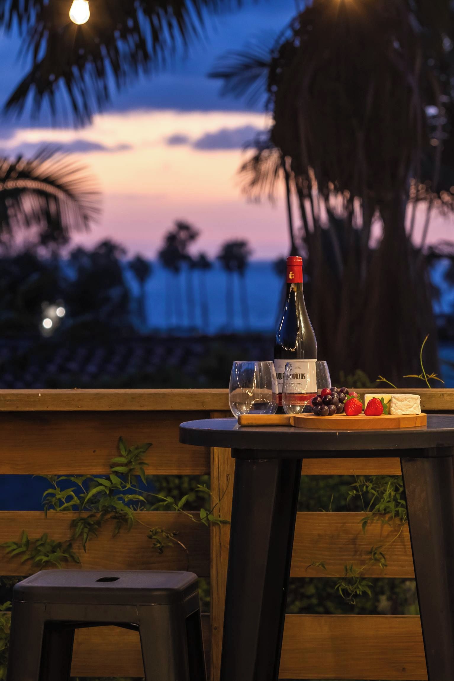 A table with a bottle of wine, glasses, and a cheese board with grapes and strawberries.