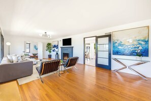 A modern living room with a fireplace, a dining area, and a large painting on the wall. - The Shores House,  Walk to Beach & Fire Pit (San Diego)