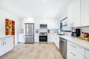 A modern kitchen with white cabinetry, stainless steel appliances, and a wooden floor. - The Shores House,  Walk to Beach & Fire Pit (San Diego)