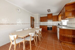 Une cuisine avec une table et des chaises, des meubles de rangement en bois, une horloge et un pare-feu en carreaux.