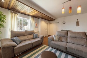 Ein Wohnzimmer mit zwei Sofas, einem Streifenmuster-Teppich und einer Decke mit Holzbalken und Pendelleuchten.