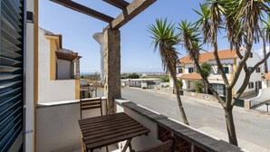 Een balkon met een houten tafel en stoelen, met uitzicht op een straat met huizen en palmbomen.