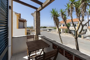 Ein Balkon mit Holztisch und Stühlen, mit Blick auf eine Straße mit Häusern und Palmen.