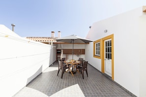 A patio with a table and chairs, a hanging chair, and a brick oven. - Casa Onda Perfeita - Sunny Terrace (Peniche)