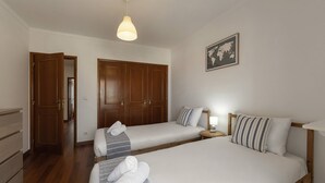 Een hotelkamer met twee bedden, een houten garderobe, een hanglamp en een wereldkaart aan de muur.