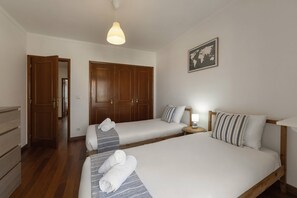 Ein Hotelzimmer mit zwei Betten, einem Holzschrank, einer Pendelleuchte und einer Weltkarte an der Wand.