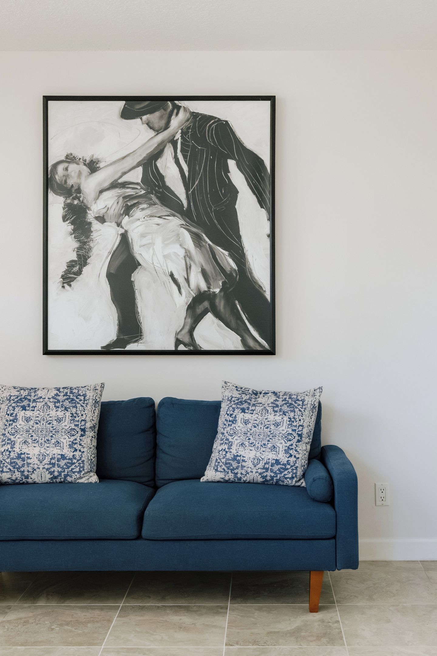 Ein gerahmtes Schwarz-Weiß-Kunstwerk über einer blauen Couch mit gemusterten Kissen.