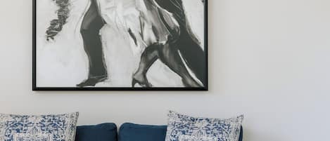 Ein gerahmtes Schwarz-Weiß-Kunstwerk über einer blauen Couch mit gemusterten Kissen.