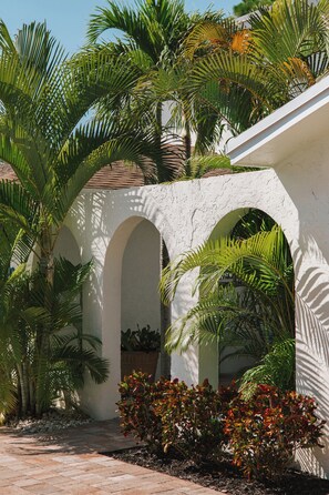 A courtyard with palm trees, a white building with arches, and a brick pathway. - Heated Pool, Close to Downtown Delray, Six-Bedroom Estate! (Delray Beach)