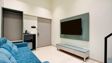 Una sala de estar moderna con un televisor de pantalla plana grande montado en la pared, un sofá azul y un mueble bajo para entretenimiento con una cafetera.