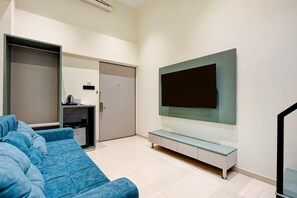 A modern living room with a large flat-screen TV mounted on a wall, a blue sofa, and a small entertainment unit with a coffee machine.
