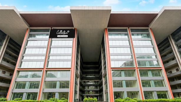 A modern building with a central atrium, large windows, and a sign indicating it is a collection of serviced apartments. - Suite Room Hotel Nano Pod (Surat)