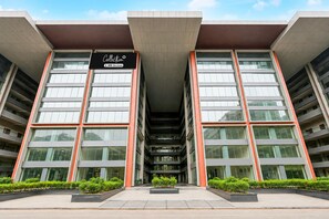 A modern building with a central atrium, large windows, and a sign indicating it is a collection of serviced apartments.