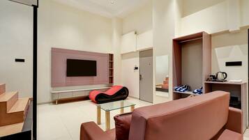 Una sala de estar moderna con un televisor de pantalla plana montado en la pared, una mesa de centro de vidrio y una zona de estar con sofá y una silla roja.