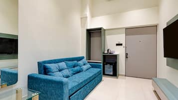 Una sala moderna con un sofá azul, una mesa de centro de vidrio, un televisor de pantalla plana y una pequeña área de kitchenette.