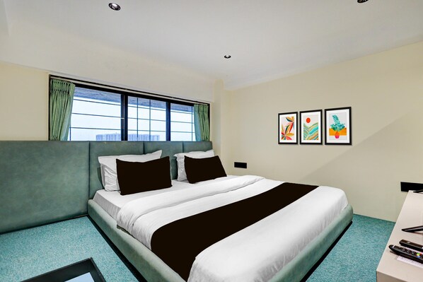 A hotel room with a bed, a window with curtains, and three framed artworks on the wall.