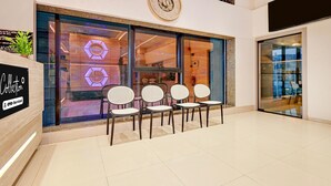A modern interior with a reception area featuring a clock, seating, and a sign indicating OYO-Service. - Suite Room Hotel Nano Pod (Surat)