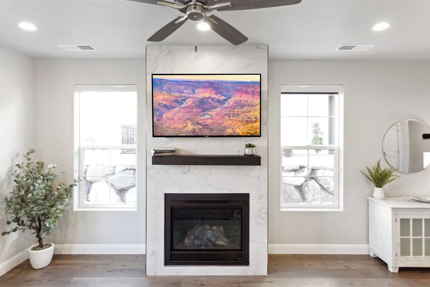 A living room with a fireplace, a mounted TV, and a ceiling fan.