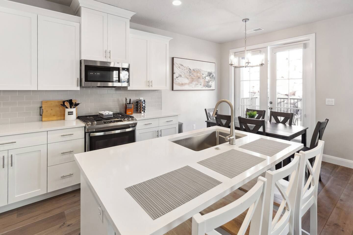 A modern kitchen with white cabinetry, a stainless steel stove, and a large island with a sink.
