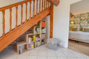A staircase with wooden balusters leading to a lower level, a bookshelf with various items, a small bench, and a bed with a white cover in a room with a tropical wallpaper. - A l'Aube des Lacs - LUSIGNY SUR BARSE (LUSIGNY SUR BARSE)