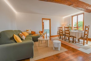 Ein Wohnzimmer mit einer Couch, einem Esstisch mit Stühlen und einem kleinen weißen Hocker.
