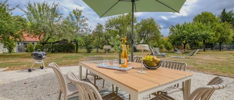Un espace extérieur aménagé pour les repas, avec une table, des chaises, un barbecue et un parasol.