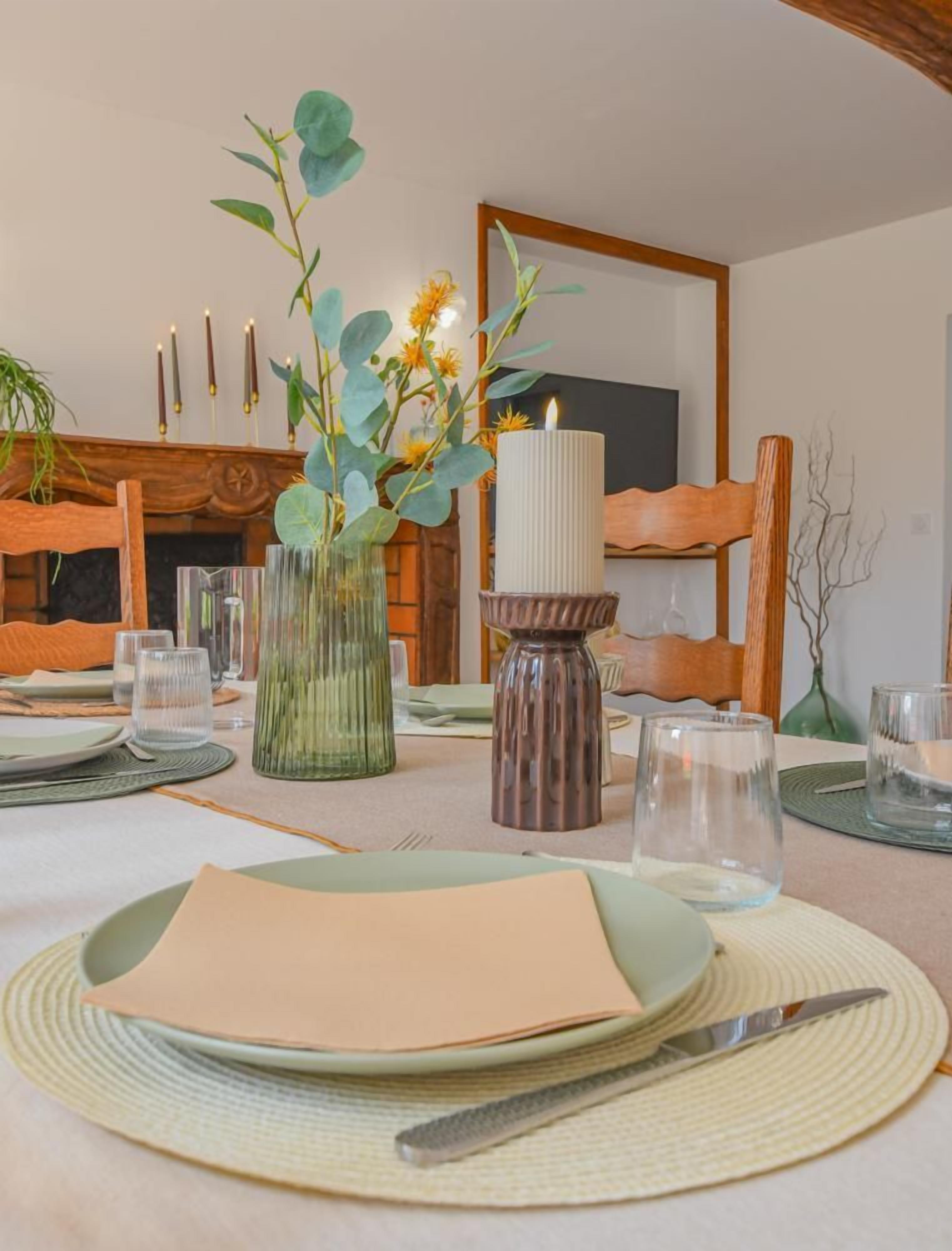 Mesa de comedor servida con platos, cubiertos, vasos y velas, con un florero y un candelabro en el centro.
