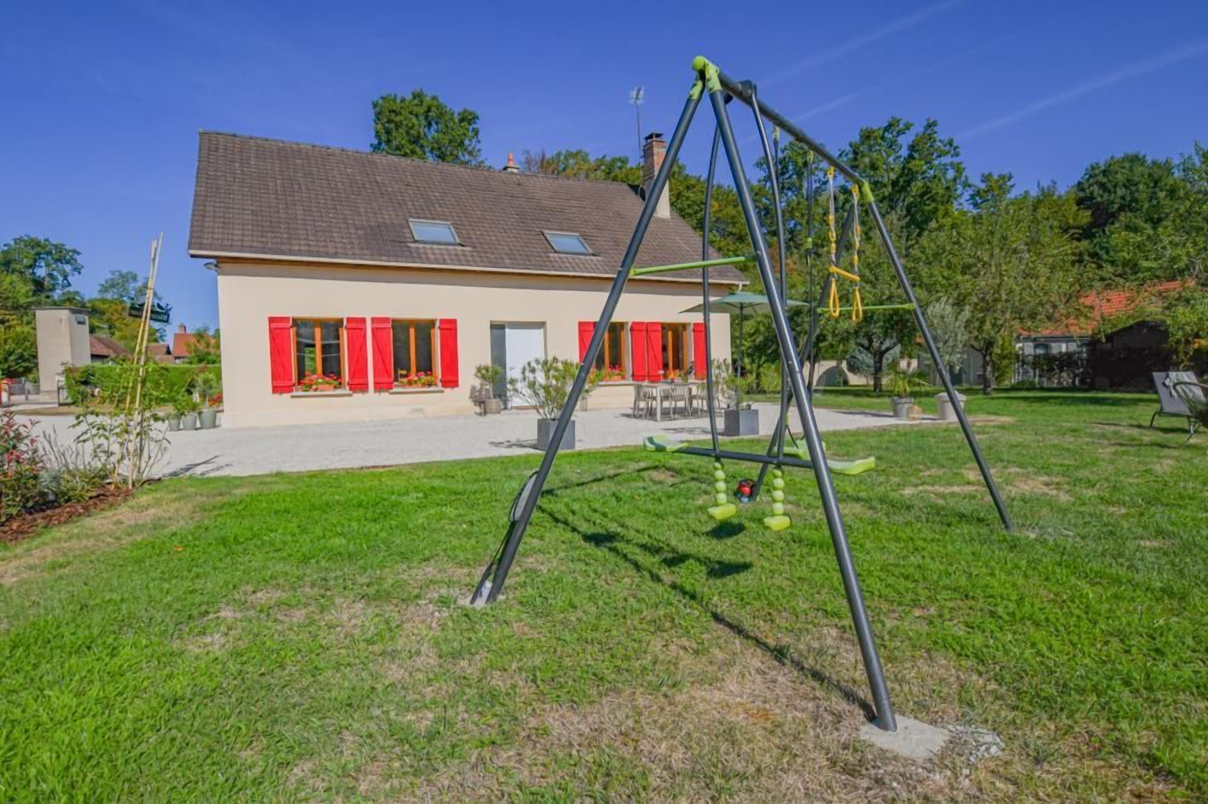 Une maison avec une balançoire dans le jardin.