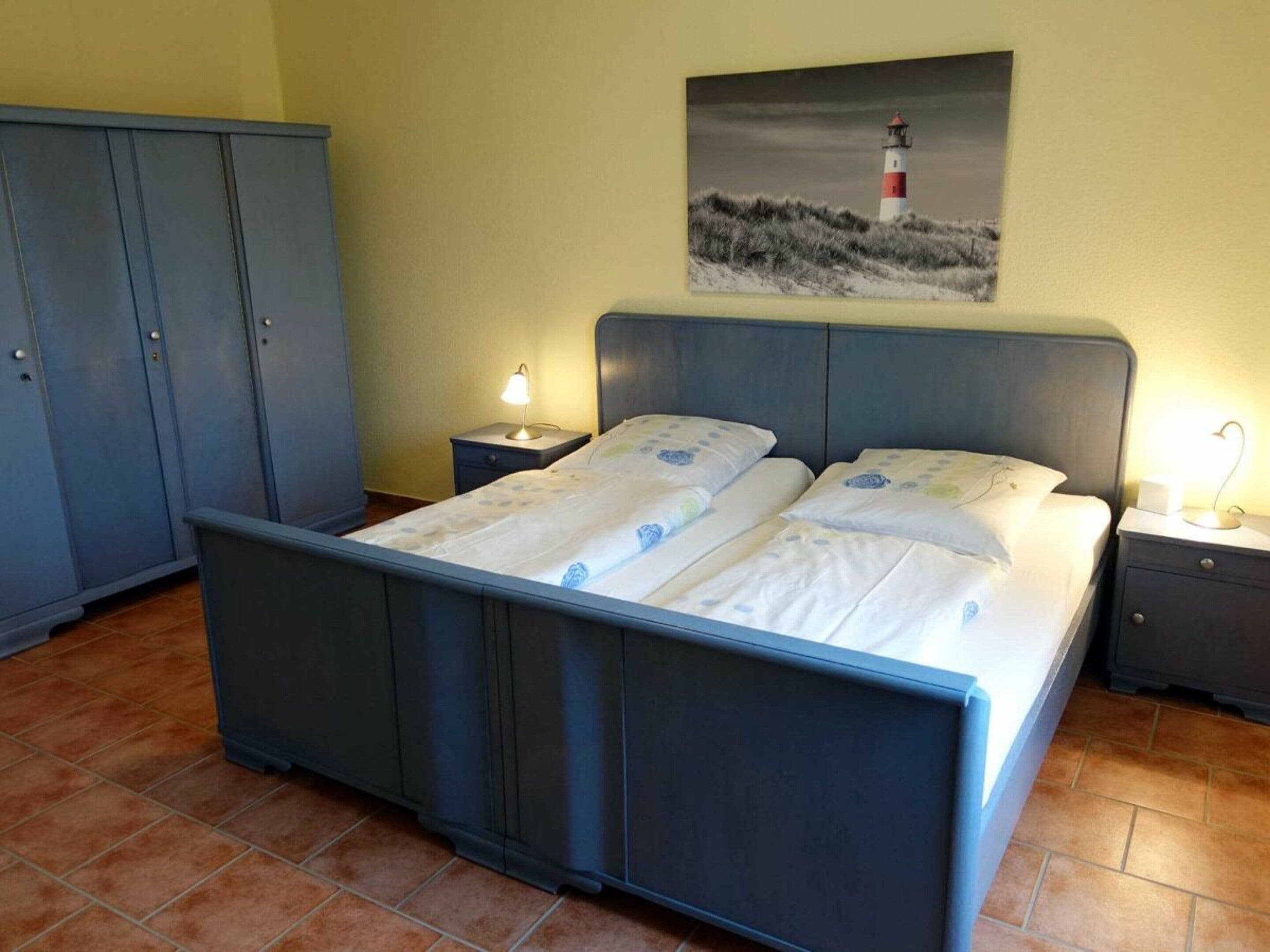 Une chambre à coucher comprenant un lit, deux tables de chevet, une commode, une armoire et un tableau représentant un phare.