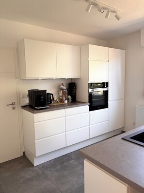 A modern kitchen with white cabinetry, a built-in oven, and a coffee machine on the countertop.
