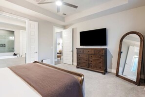 A bedroom with a bed, dresser, TV, and a large mirror. - Easton Park 4BR with Private Resort-Style Pool (Austin)