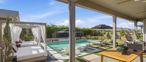 A covered outdoor area with a pool, lounge chairs, and a table.