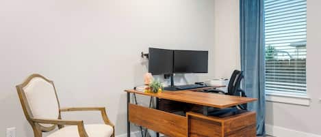 Een moderne kantoorruimte met een houten bureau, een stoel, een flatscreen monitor en een raam met jaloezieën.