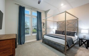 Ein Bett mit Himmelbett, ein Nachttisch mit Lampe, eine Holzkommode und ein Fenster mit Vorhängen.