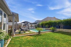 A residential backyard with a swimming pool, a covered patio area, and a well-maintained lawn. - Easton Park 4BR with Private Resort-Style Pool (Austin)