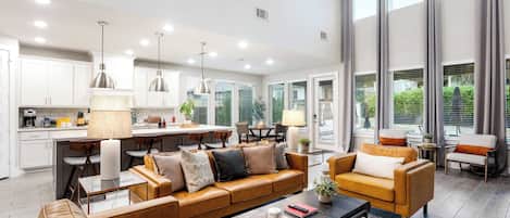 A modern living room with a brown leather sofa, a coffee table, and a dining area with a kitchen in the background.