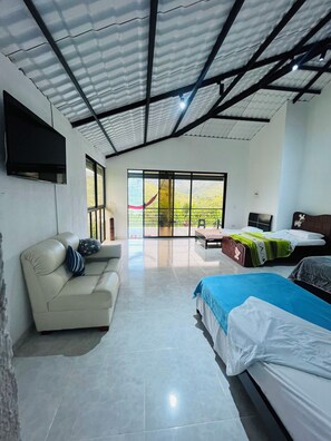 A room with a sofa, a bed, and a large window with a view of greenery.