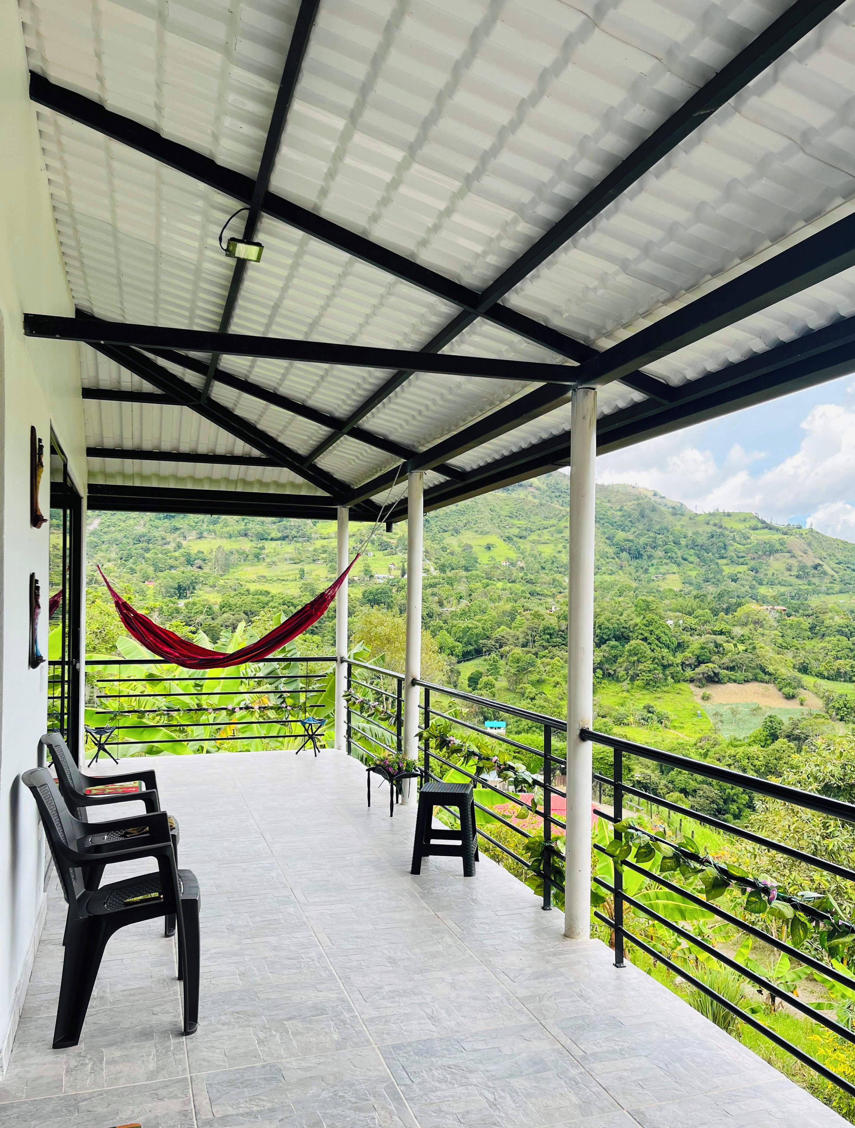 Une terrasse couverte, dotée de chaises et d’un hamac, qui offre une vue sur un paysage luxuriant.