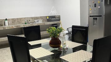 A modern kitchen with a glass dining table, chairs, a refrigerator, and a plant.